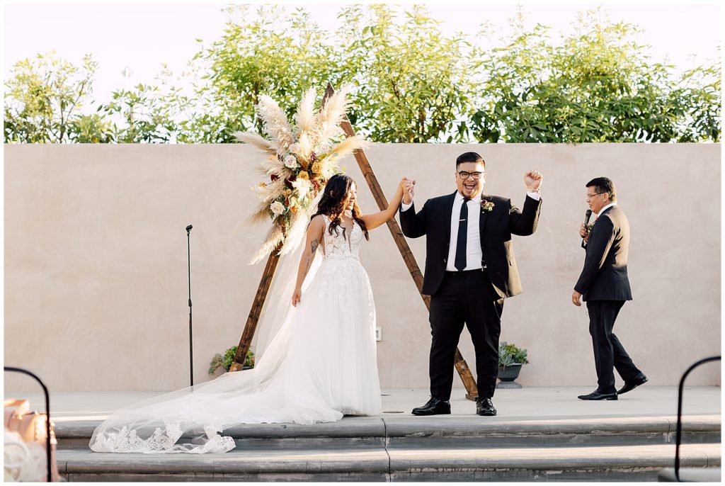 bride and groom getting married in front of triangle ceremony arch with pampas grass floral arrangement