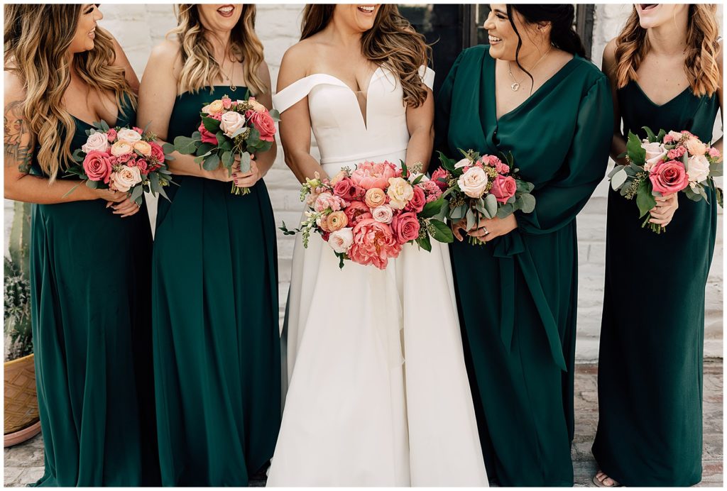 bride and bridesmaids holding pink, blush, and coral wedding bouquets with coral charm peonies and eucalyptus. bridesmaids wearing long emerald green dresses