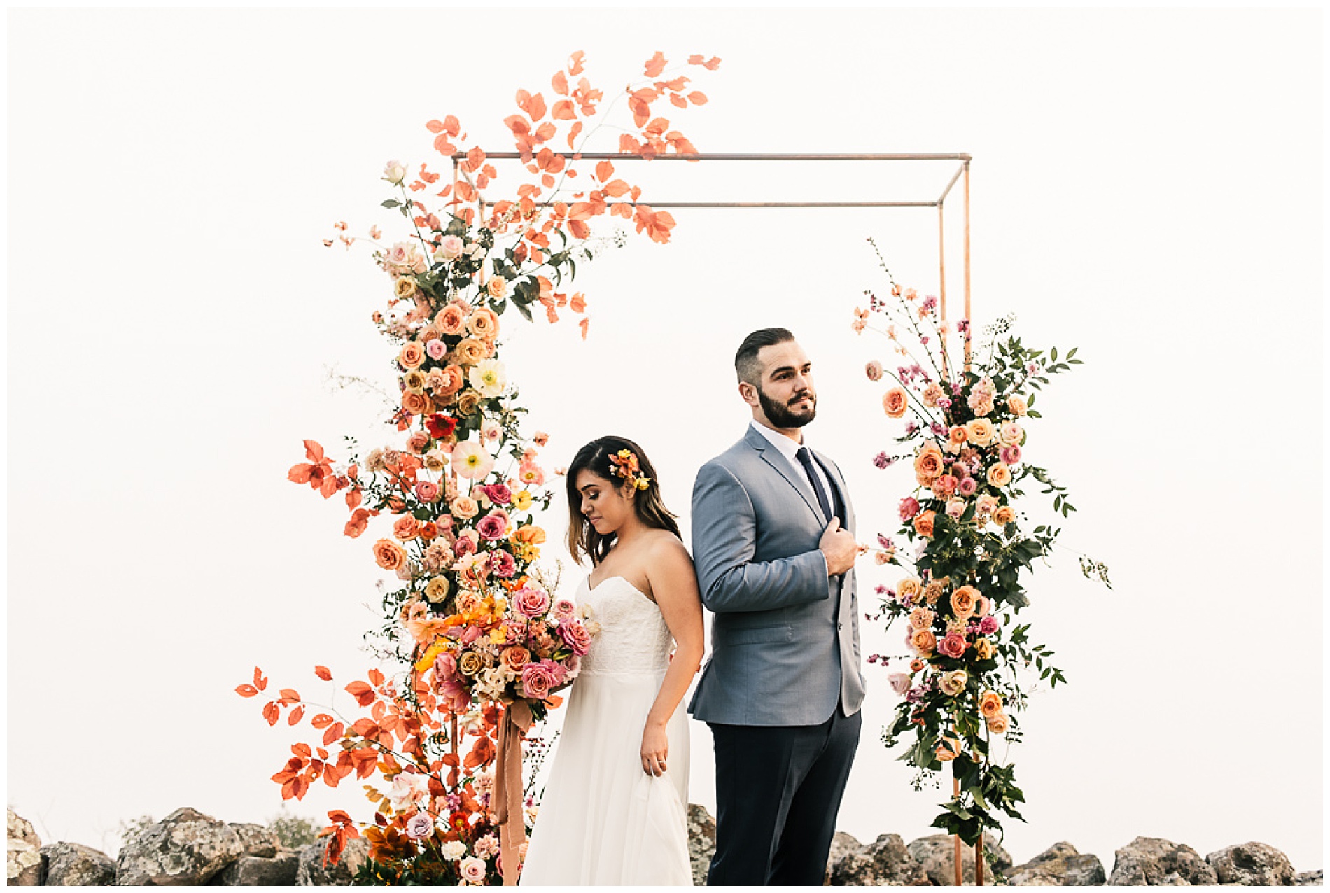 bride and groom standing in front of colorful ceremony arch floral installation