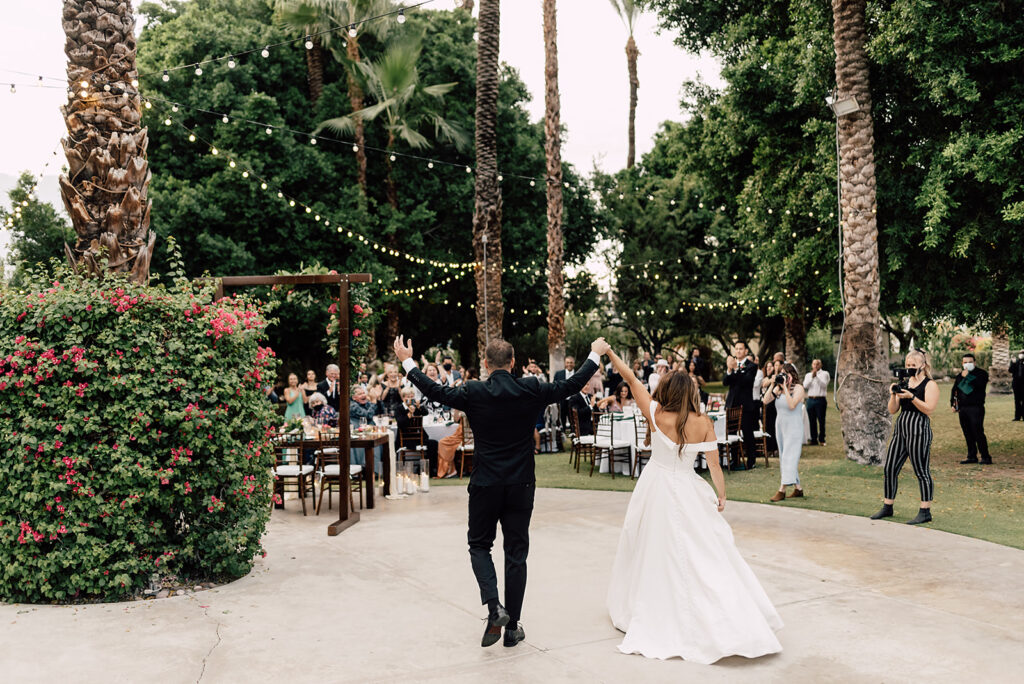 Bride and Groom walking into receptions at their wedding with hands up in the air, while their guess cheer and clap for them. 