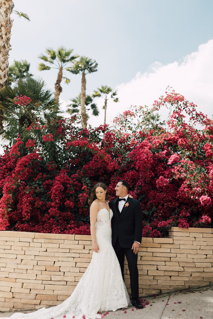 Bride and Groom standing next to each other smiling in front of flower wall at Indian Wells Golf Course In Palm Springs, California