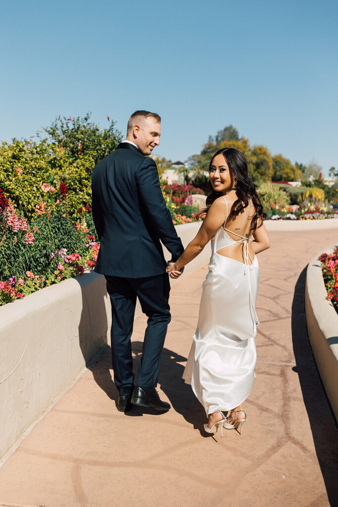 Bride and groom walking hand-in-hand  next to flowers. 
